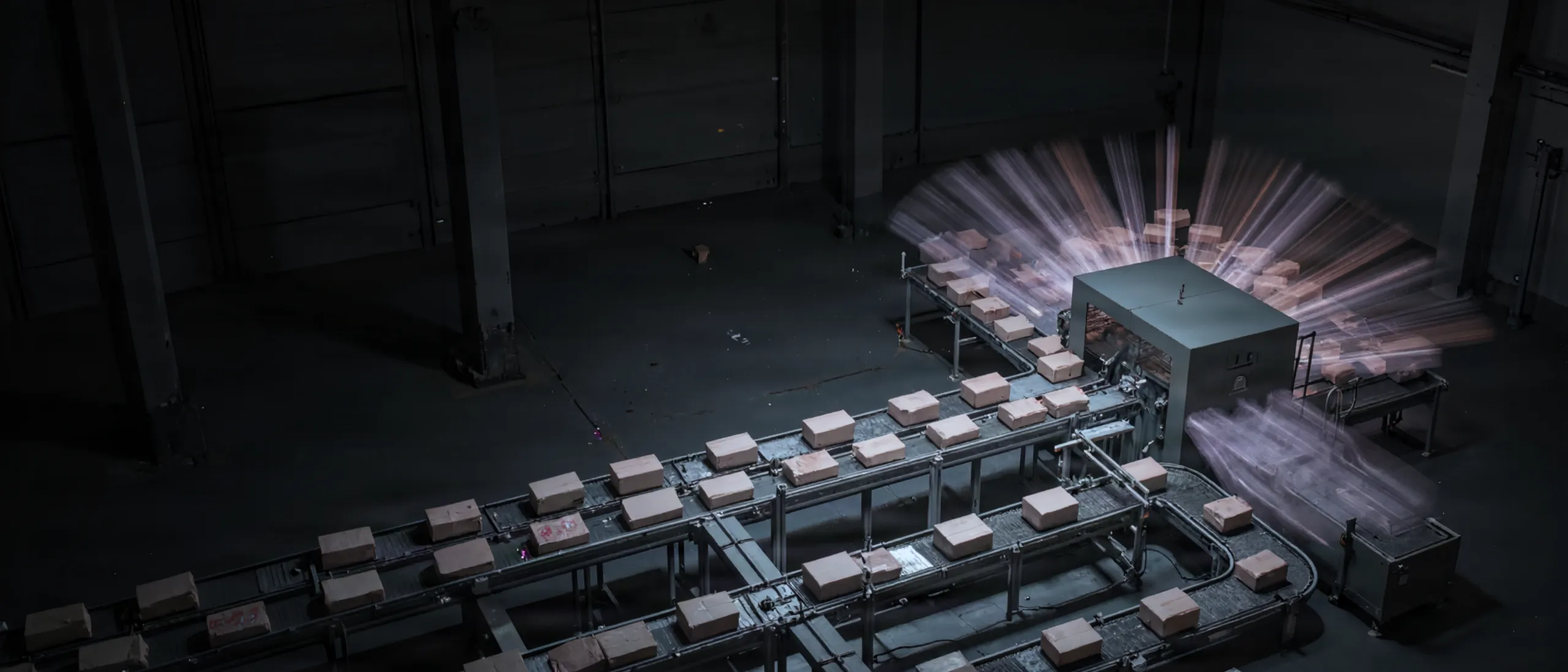 A logistics hall at night from above: parcels on several conveyor belts converge at one single station, where they blur into light trails.
